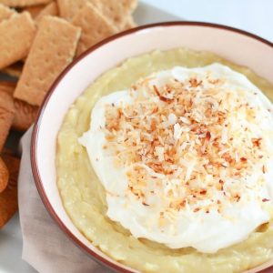 Bowl of coconut pie dip topped with whipped cream and toasted coconut.