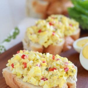 Egg salad on a piece of bread on a wooden board.