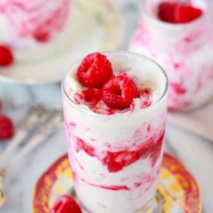 Glass filled with layers of whipped cream and raspberries.