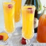 Three mimosas in champagne glasses garnished with a raspberry.