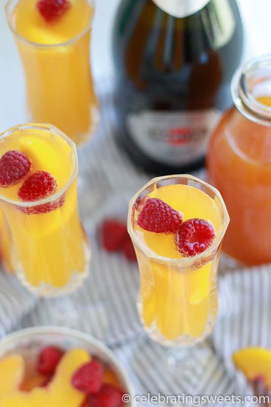 Three mimosas in champagne glasses garnished with raspberries.