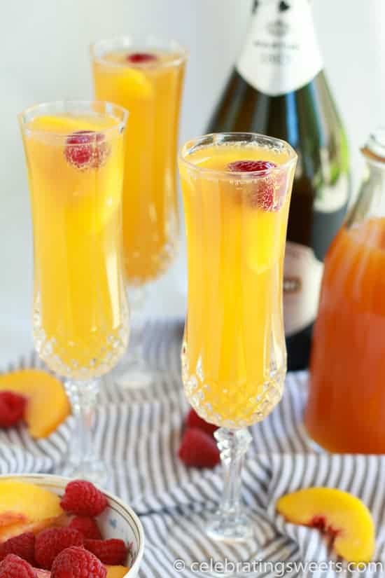 Three mimosas in champagne glasses garnished with a raspberry.