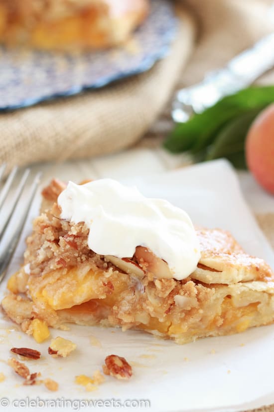 Slice of peach galette on a white plate topped with whipped cream.