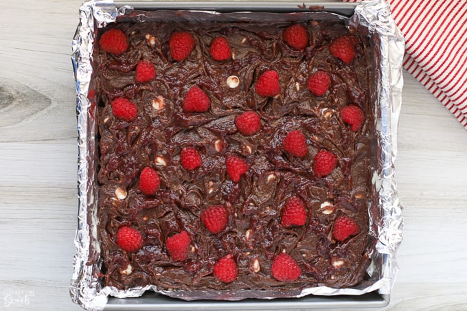 Brownie batter in a square pan topped with raspberries. 