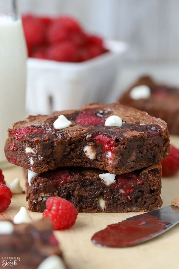 Two raspberry brownies stacked on top of each other with a bowl of raspberries in the background. 