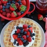 White plate with waffles, berries, and whipped cream.