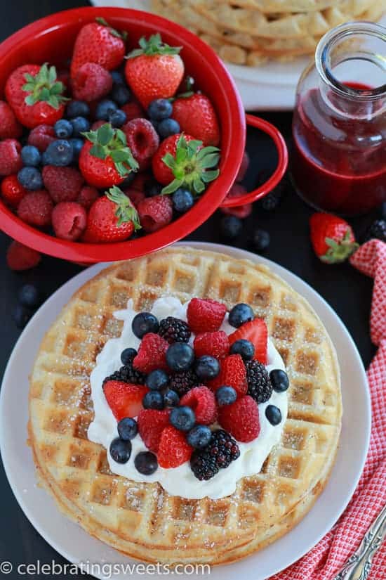 White plate with waffles, berries, and whipped cream.