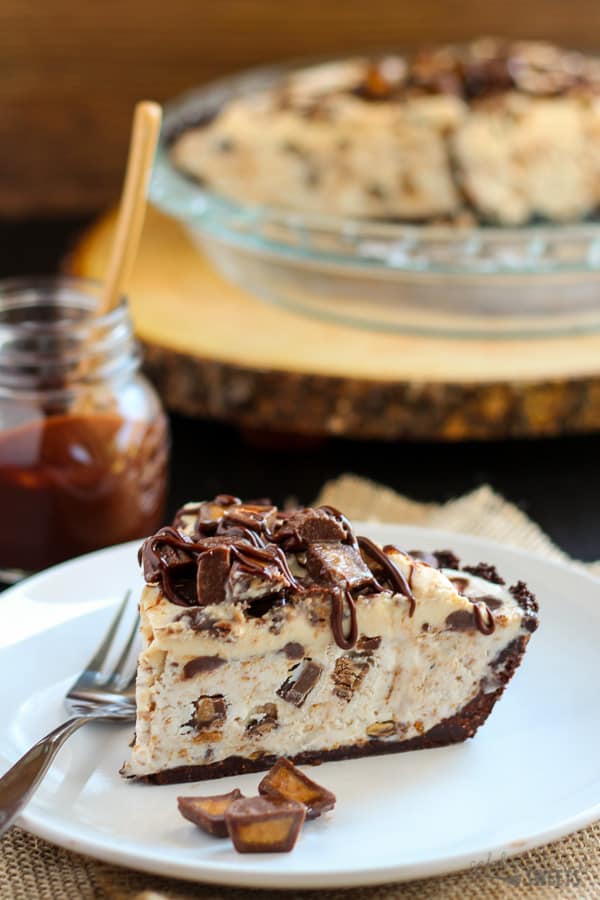 Slice of peanut butter ice cream pie topped with fudge sauce and chopped peanut butter cups.