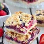Two berry crumb bars on a board with berries in the background.