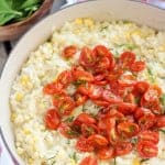 Corn risotto in a pan topped with roasted cherry tomatoes.
