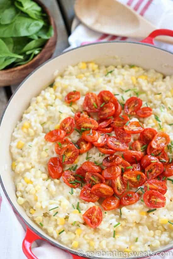 Corn risotto in a pan topped with roasted cherry tomatoes. 