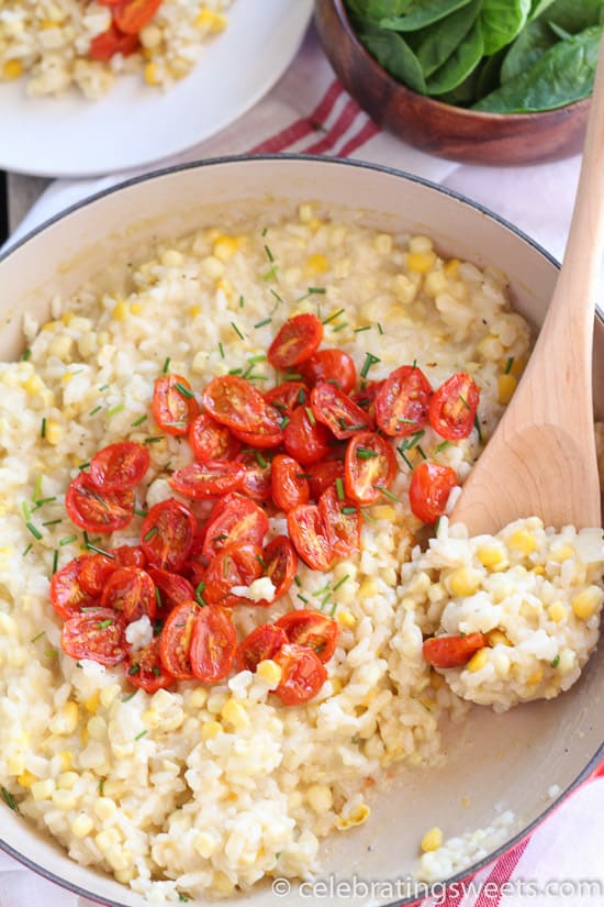 Corn risotto in a pan topped with roasted cherry tomatoes. 