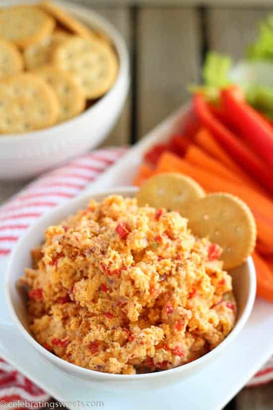 White bowl filled with pimento cheese garnished with crackers and vegetables. 