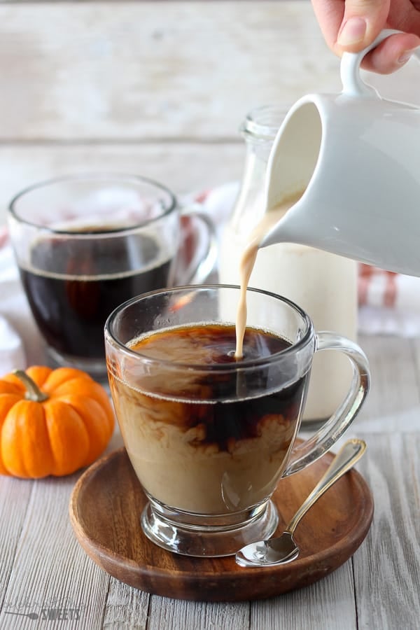 Tasse Kaffee mit Creamer, der hineingegossen wird.