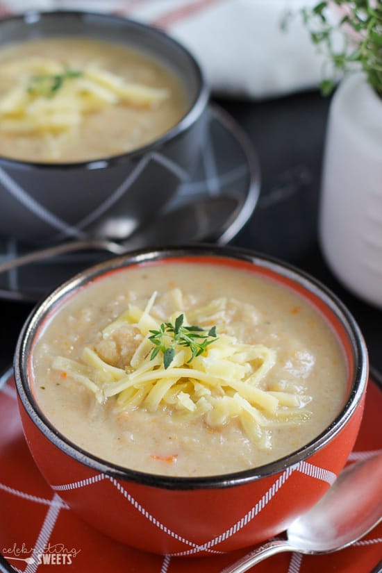 Cauliflower soup in red and grey bowls topped with white cheddar.
