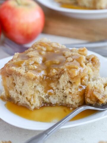 A slice of apple cake on a white plate topped with caramel sauce.