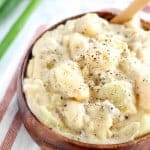 Cheesy potatoes in a wooden bowl topped with ground pepper.