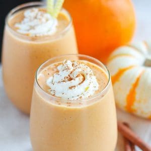 Pumpkin smoothie in a glass topped with whipped cream and cinnamon.