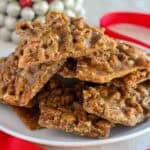 Pecan praline toffee piled on a white plate next to a red ribbon.