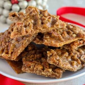 Pecan praline toffee piled on a white plate next to a red ribbon.