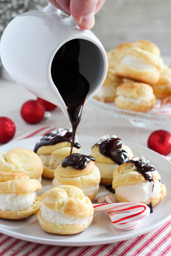 Pouring chocolate sauce over cream puffs on a white plate.