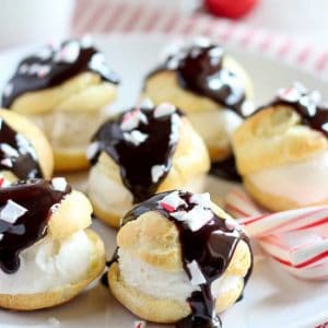 Cream puffs covered in chocolate on a white plate.
