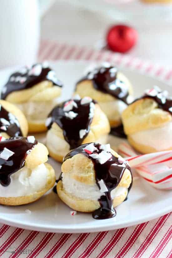 Cream puffs covered in chocolate on a white plate.
