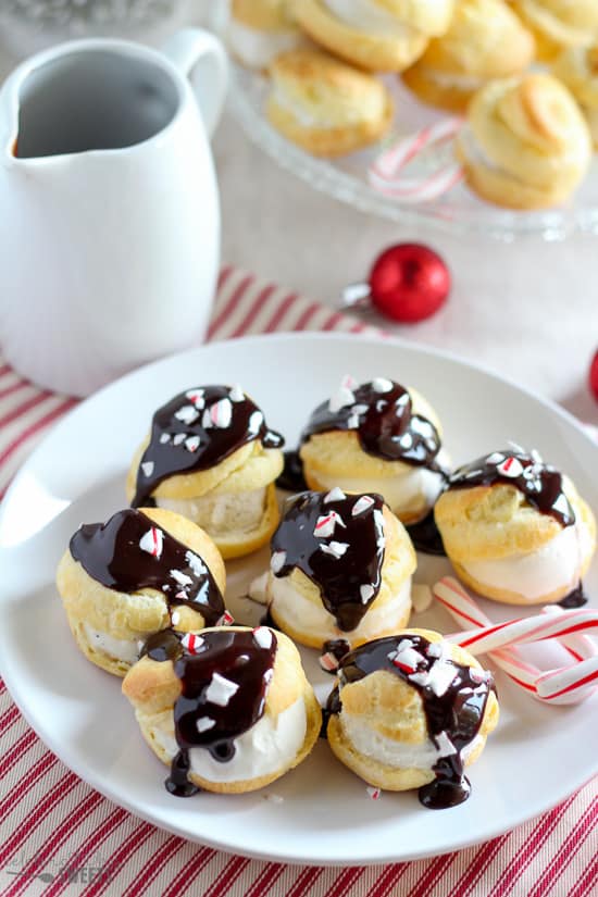 Creams puffs topped with chocolate sauce on a white plate.