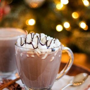 Glass of hot chocolate topped with marshmallows and a drizzle of chocolate sauce.