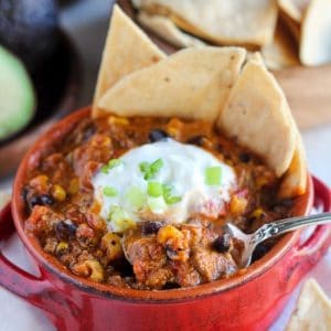 Taco soup in a red bowl with chips and sour cream.
