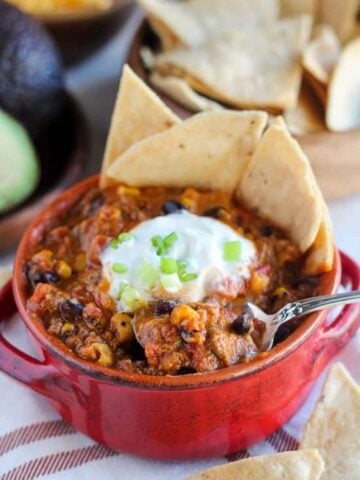 Taco soup in a red bowl with chips and sour cream.