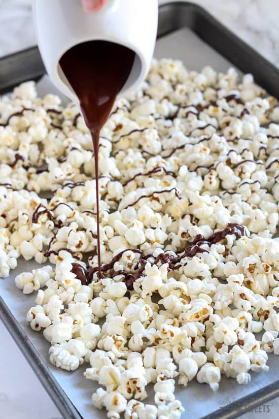 Tray of popcorn being drizzled with melted dark chocolate