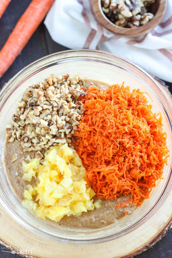 Cake batter in a glass bowl with grated carrots, pineapple, and nuts.