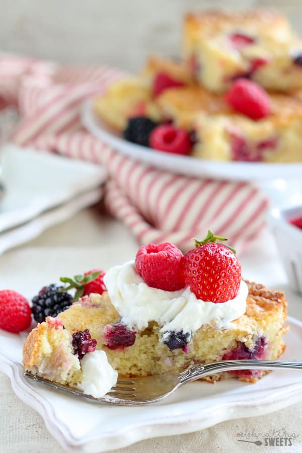 Slice of berry cake topped with whipped cream and berries.