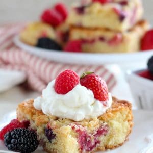 Close up of a slice of berry cake topped with whipped cream and berries.