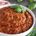 Meat sauce in a white bowl garnished with basil.