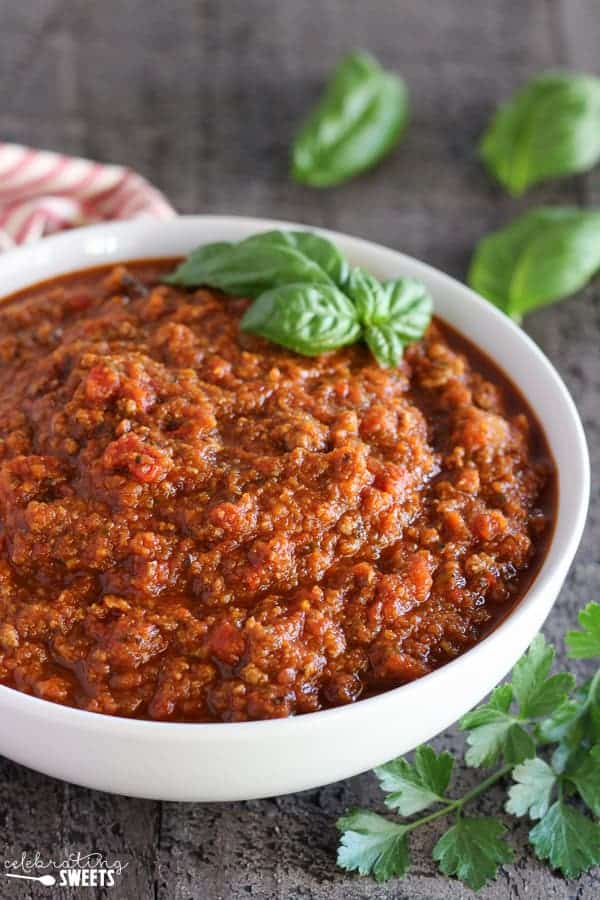 Meat sauce in a white bowl garnished with basil. 