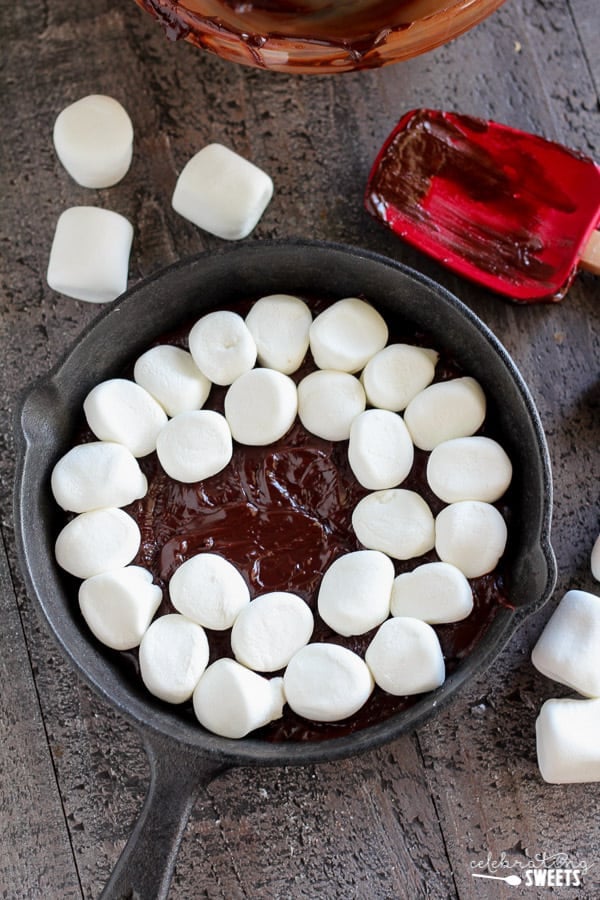 Marshmallows on top of melted chocolate in a skillet.
