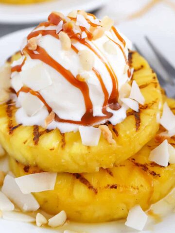 Grilled pineapple on a white plate topped with ice cream.