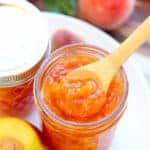 Closeup of peach jam with a wooden spoon.