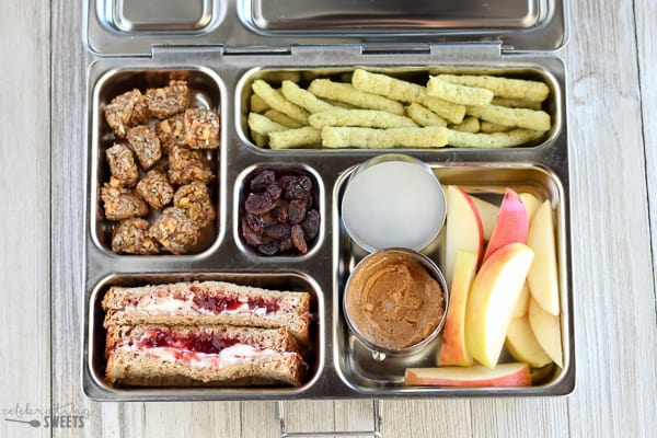 Lunchbox with apples, sandwich, granola, and chips.
