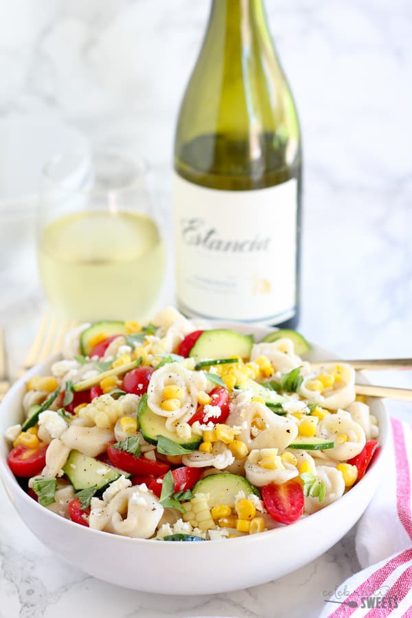 Bowl of tortellini pasta salad with wine in the background. 