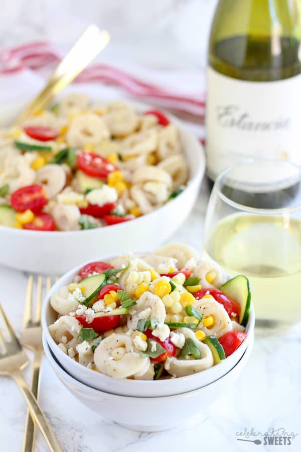 Bowl of tortellini pasta salad with wine in the background. 