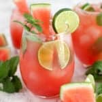 Pink Watermelon Mojitos in a glasses garnished with mint, lime, and watermelon.