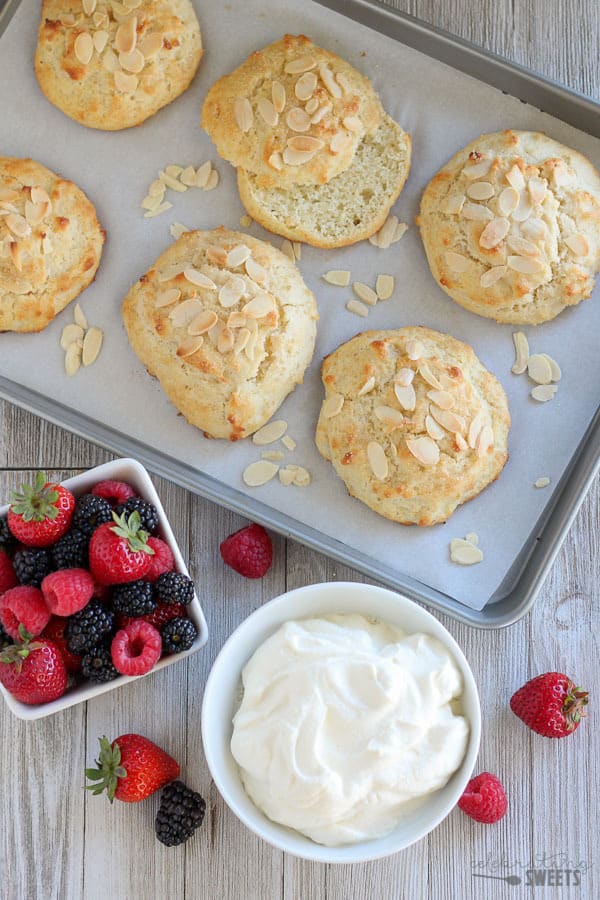 shortcakes on a cookie sheet with a bowl of whipped cream and berries. 