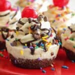 Ice cream cupcake topped with sundae toppings on a red plate.