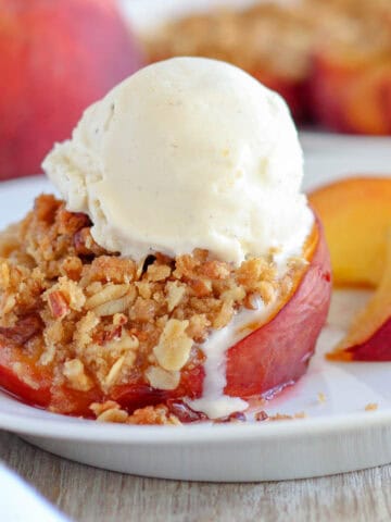 A stuffed peach on a white plate topped with a scoop of ice cream.