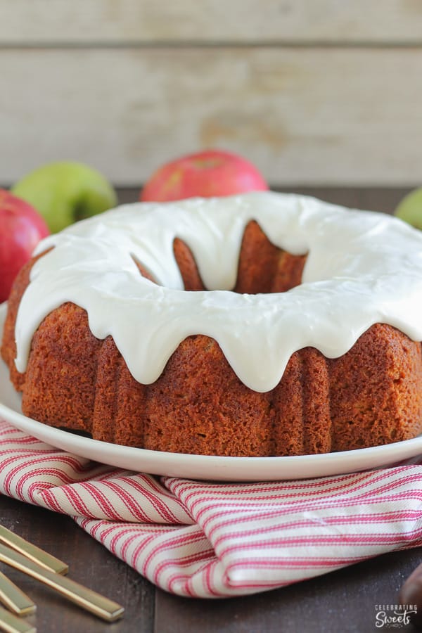 Apple bundt cake topped with cream cheese glaze on a white plate and a red striped napkin.