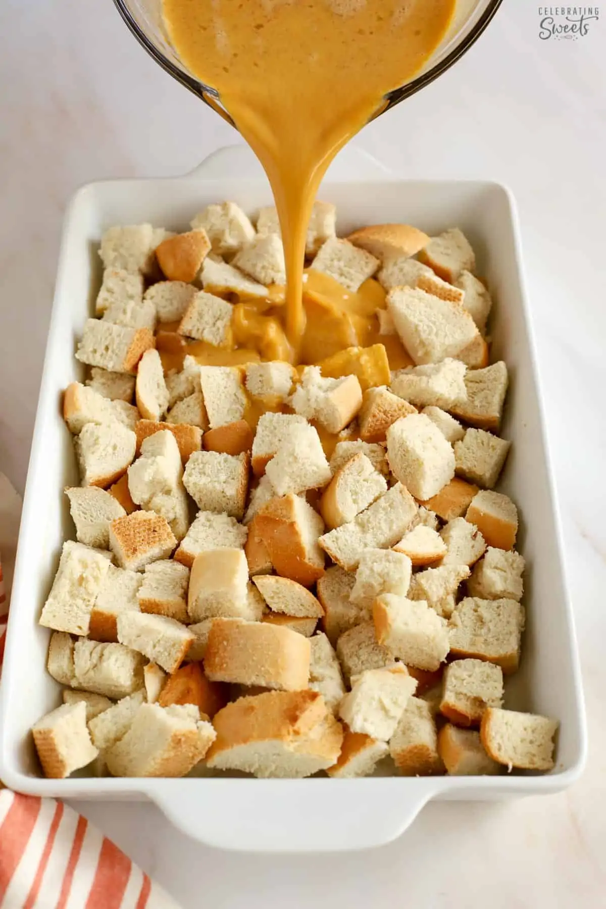 Pumpkin custard being poured over bread cubes in a casserole dish.