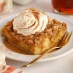 Slice of pumpkin french toast casserole on a white plate topped with whipped cream and cinnamon